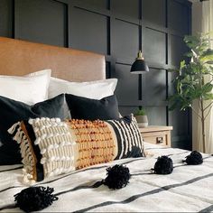 a bed with black and white pillows on top of it next to a potted plant