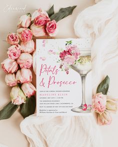 an elegant wedding card with pink flowers and greenery on the table next to it