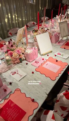 the table is set up with pink and red flowers, cards, candles, and other items