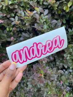 someone holding up a sticker with the word andreee on it in front of some bushes