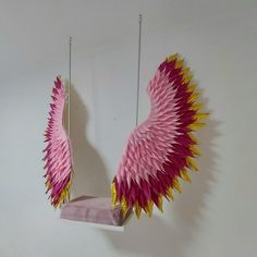 pink and yellow wings hanging from strings on a white wall next to a bed frame