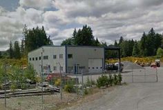 an industrial building sitting on the side of a road next to some trees and bushes