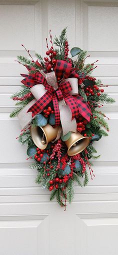 a christmas wreath hanging on the front door with two bells and evergreen leaves, red berries, and white ribbon