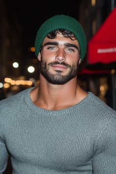 a man with a beard wearing a green beanie and looking at the camera while standing in front of a building