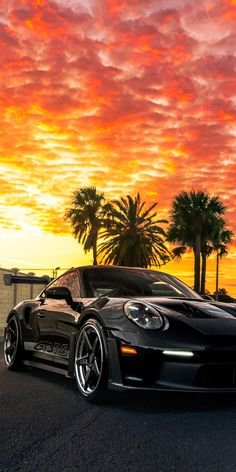 a black sports car parked in front of a palm tree with the sun setting behind it