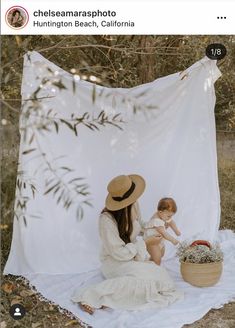 a woman sitting on top of a blanket holding a baby