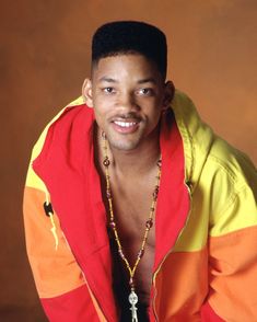 a man in an orange, yellow and red jacket posing for a photo with his hands on his hips