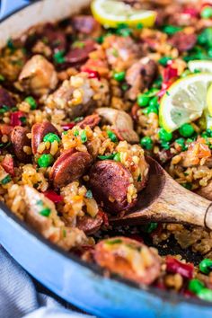 a pan filled with rice, peas and sausage next to a lemon wedge on the side