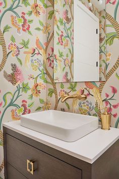 a bathroom sink sitting under a mirror next to a wall papered with colorful flowers