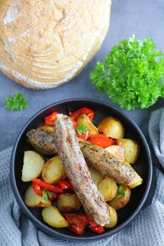 a bowl filled with sausage, potatoes and carrots next to a loaf of bread