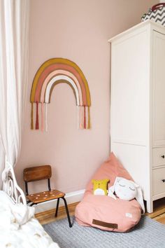 a bedroom with pink walls, white furniture and a rainbow wall hanging above the bed