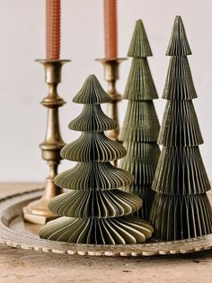 three small christmas trees sitting on top of a wooden table next to candlesticks