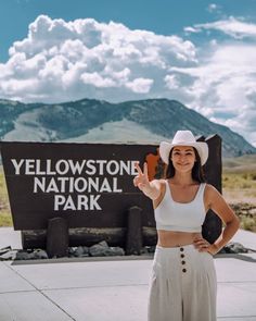 a woman standing in front of the yellowstone national park sign wearing a white cowboy hat