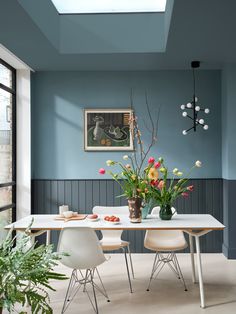 a dining room with blue walls and flowers in vases on the table next to two chairs