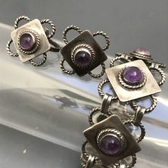 "Vintage ~ Pre eagle mark ~ sterling silver linked panel bracelet and matching screw-back earrings ~ Each panel has a bezel set amethyst cab in center with applied wire work around it ~ Bracelet ends with a simple \"J\" hook clasp ~ Very well made piece with beautiful details . Marked Silver Mexico on the backside . Measurements : Bracelet is 7 3/4 inches x 7/8 inches max width . Earrings are 7/8 inches x 7/8 inches Weighs 47 grams on my weighing scale . Condition : Overall Good vintage conditio Modernist Metal Jewelry, Modernist Metal Pierced Jewelry, Vintage Amethyst Jewelry With Polished Finish, Adjustable Modernist Bracelet, Collectible Silver Jewelry With Matching Earrings, Adjustable Modernist Sterling Silver Jewelry, Modernist Formal Jewelry Stamped 925, Modernist Stamped 925 Jewelry For Formal Occasions, Amethyst Silver Jewelry With Polished Finish