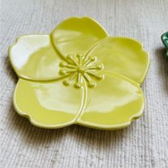 two yellow and green flower shaped dishes on a white tableclothed surface next to each other