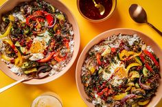 two bowls filled with rice, vegetables and sauces on top of a yellow table