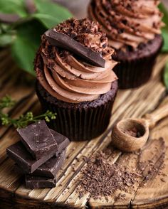 two cupcakes with chocolate frosting on a wooden table next to some leaves