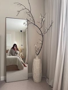 a woman sitting on a bed in front of a large mirror with flowers and branches