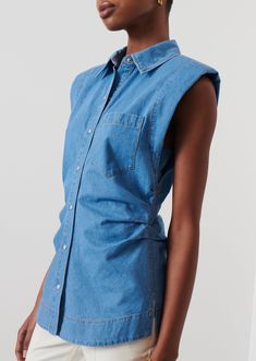 The Ivy Sleeveless Ruched Button Down Shirt is done in a soft washed indigo chambray in light blue. It features a spread collar, buttons along the front placket and extended shoulders with shoulder pads. The silhouette is slightly tailored at the waist with side seam pleats and extends to a curved hem with shirttail. It is finished with a single front patch pocket.This style runs small. Please size up. Sleeveless Button Up Shirt, Runching Shirt, Shirt Trend 2024, Ruched Shirt, Drape Top, Sleeveless Button Down Shirt, Embellished Shirt, Chambray Top, Denim Ideas