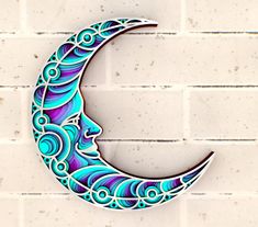 a metal crescent moon with blue and purple swirls on it against a white brick wall