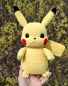 a crocheted pikachu doll is held in front of some shrubbery