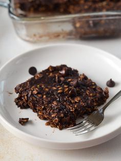 a white plate topped with a piece of chocolate cake next to a glass container filled with granola