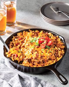 a skillet filled with macaroni and cheese next to two glasses of orange juice