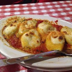 a white plate topped with ravioli and cheese covered in sauce on top of a checkered table cloth