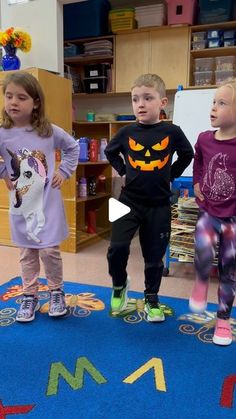 three children are standing on the floor in front of an area with letters and numbers