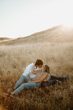 a man and woman sitting in the middle of a field with their arms around each other