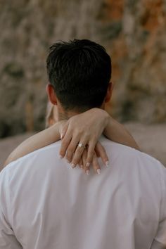 a man and woman embracing each other in front of a stone wall