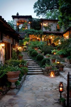 a stone path leading up to a house with lights on the steps and potted plants