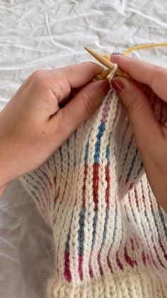 a woman knitting on a white blanket with a pair of hands holding the yarn in front of her