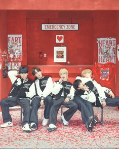 group of young men sitting on chairs in front of a red wall with hearts painted on it