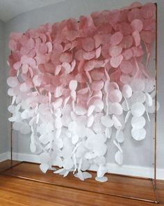 pink and white paper flowers are hanging on a metal frame in front of a wall