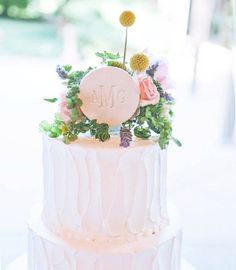 a white wedding cake with flowers and monogrammed initials on the top, sitting on a table