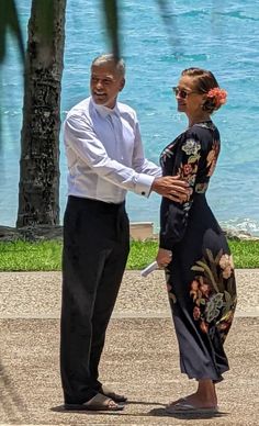 a man and woman standing next to each other near the ocean with palm trees in front of them