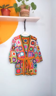 a colorful robe hanging on a wall next to a potted plant and wooden shelf