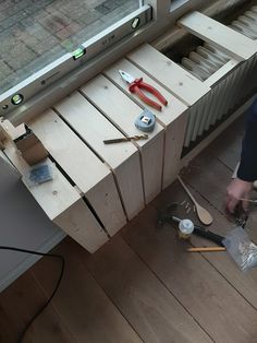 a person working on some wood with tools in front of a window and an open drawer