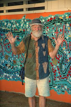 an old man standing in front of a colorful wall with his hands up to the side