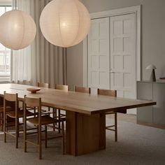 a large wooden table surrounded by chairs in a room with two lamps hanging from the ceiling