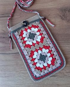 a crocheted bag with a red, white and grey design on it sitting on a wooden surface