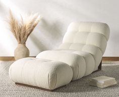 a white chair sitting on top of a rug next to a vase and a book