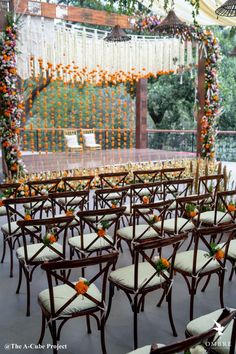 rows of chairs set up in front of an orange and white wedding arch decorated with flowers