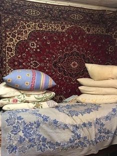 a pile of pillows sitting on top of a bed in front of a red rug