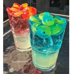 two glasses filled with different colored liquids on top of a glass table next to each other