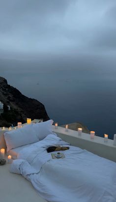 a bed with white sheets and candles on top of it next to the ocean at night