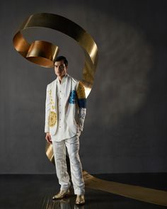 a man in a white suit and gold tie standing next to a large metal object