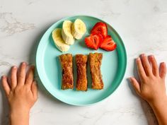 two hands on a blue plate with bananas, strawberries and other foodstuffs